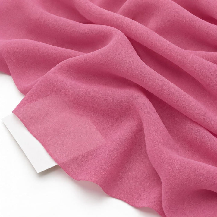 Rosa sidengeorgette – närbild med papper bakom tyget som visar att det bara är svagt genomskinligt (bild 3 av 3)